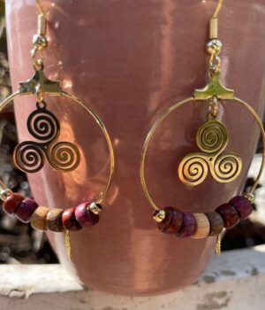 Gros plan des détails filigranés dorés des boucles d'oreilles TrisKel Lola, avec une texture élégante du bois naturel.