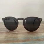 Lunettes de soleil en bois Rolling avec verres polarisés et monture en ébène et palissandre, posées sur une table en bois.