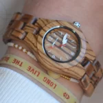 Montre Manchester en bois de zebrano pour femme, équipée d'un cadran épuré avec calendrier et trotteuse rouge, offrant une lecture facile et une touche de couleur distinctive.