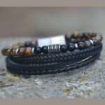 Bracelet multi-rangs en cuir noir avec pierres d'œil de tigre et d’onyx, fermoir magnétique et design artisanal.