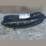 Bracelet multi-rangs en cuir noir tressé avec pierres naturelles en onyx, posé sur un socle en pierres.