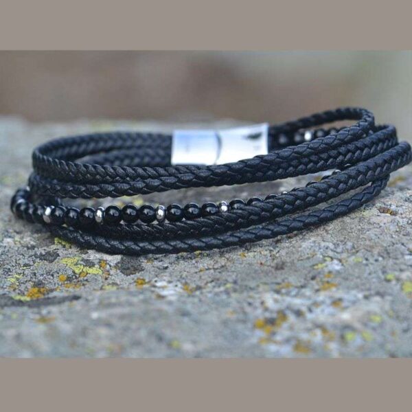 Bracelet multi-rangs en cuir noir tressé avec pierres naturelles en onyx, posé sur un socle en pierres.